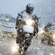 A motorbike rides through snowy traffic on a main road